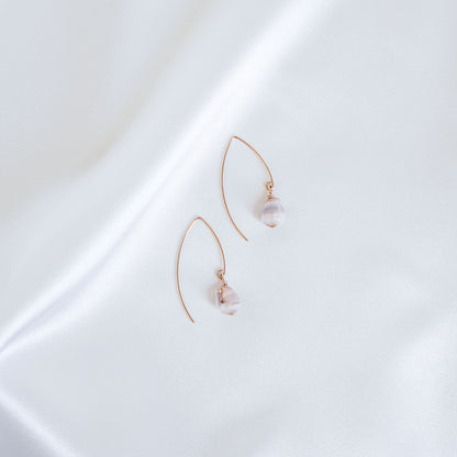 Pair of gold thread hoop earrings with tiny cone shells on a white surface