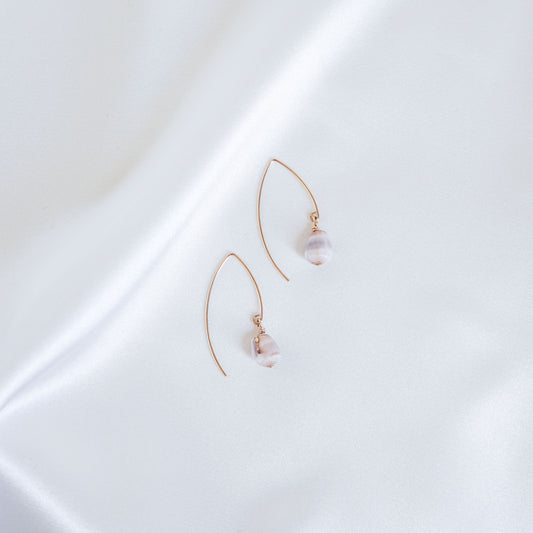 Pair of gold thread hoop earrings with tiny cone shells on a white surface
