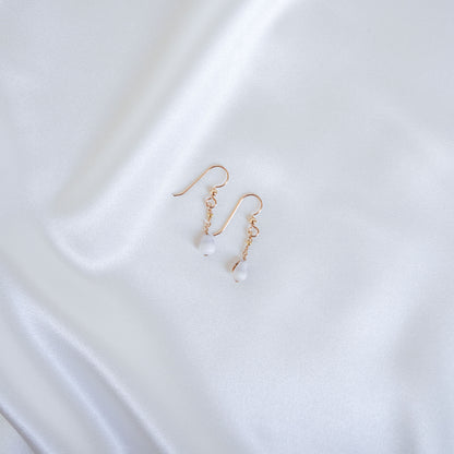 Gold short dangle earrings with white tiny cone shells on a white fabric background