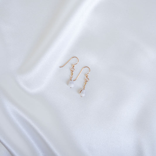 Gold short dangle earrings with white tiny cone shells on a white fabric background