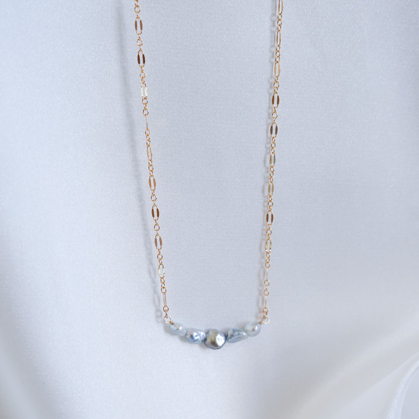 Delicate gold necklace with five small blue pearls on a white background