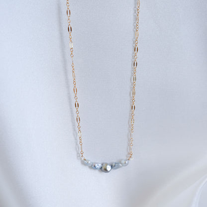 Delicate gold necklace with five small blue pearls on a white background