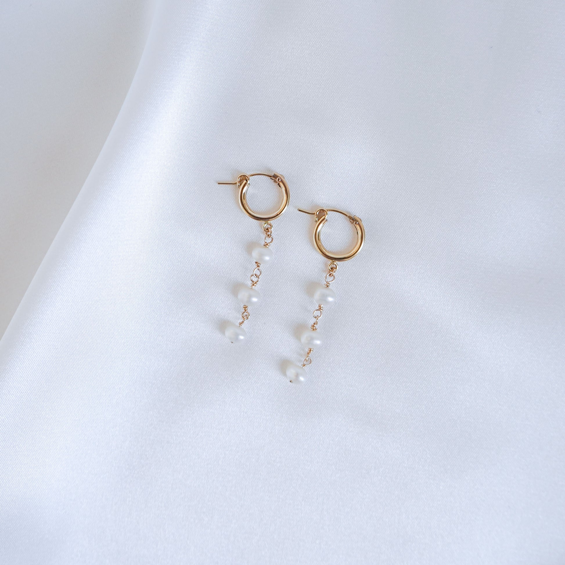 Gold hoop earrings with three pearls on a white background