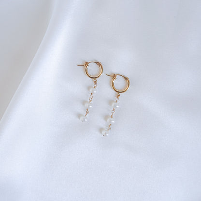 Gold hoop earrings with three pearls on a white background
