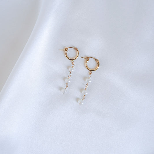 Gold hoop earrings with three pearls on a white background