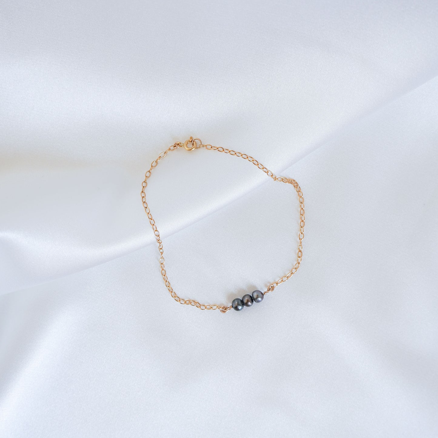 Gold bracelet with three tahitian keshi pearls on a white background