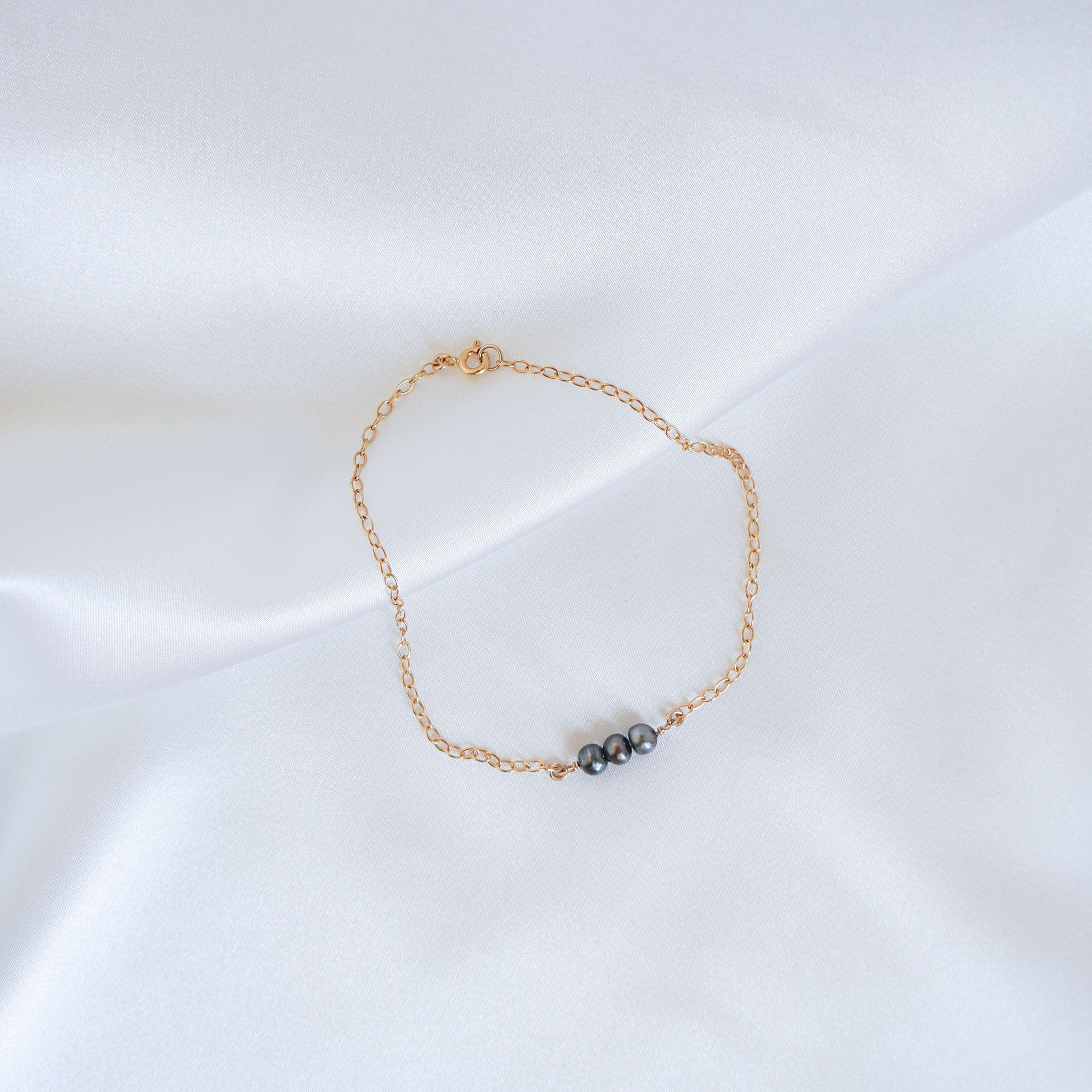 Gold bracelet with three tahitian keshi pearls on a white background