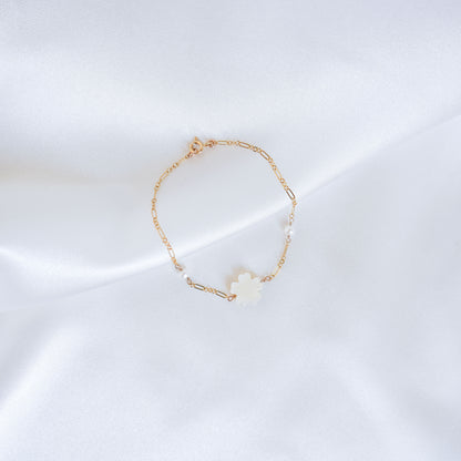 Gold bracelet with a white mother of pearl floral charm and two pearl beads on a white satin background