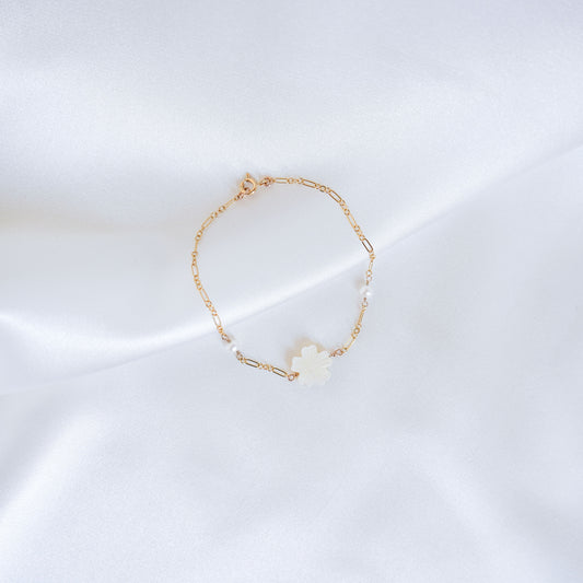 Gold bracelet with a white mother of pearl floral charm and two pearl beads on a white satin background