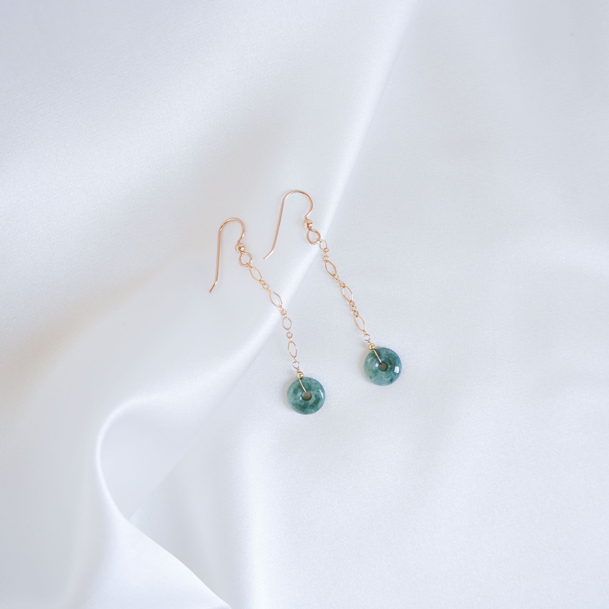 Gold dangle chain earrings with small circle jade on a white fabric background
