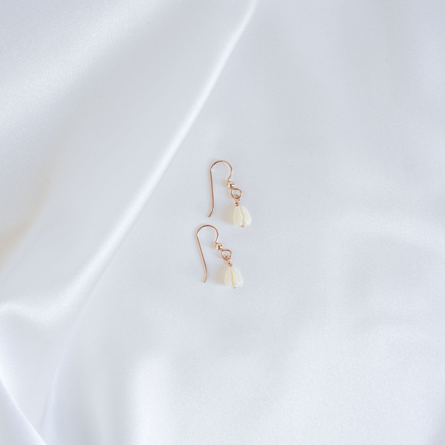Pair of gold earrings with white pikake flower beads on a white fabric background