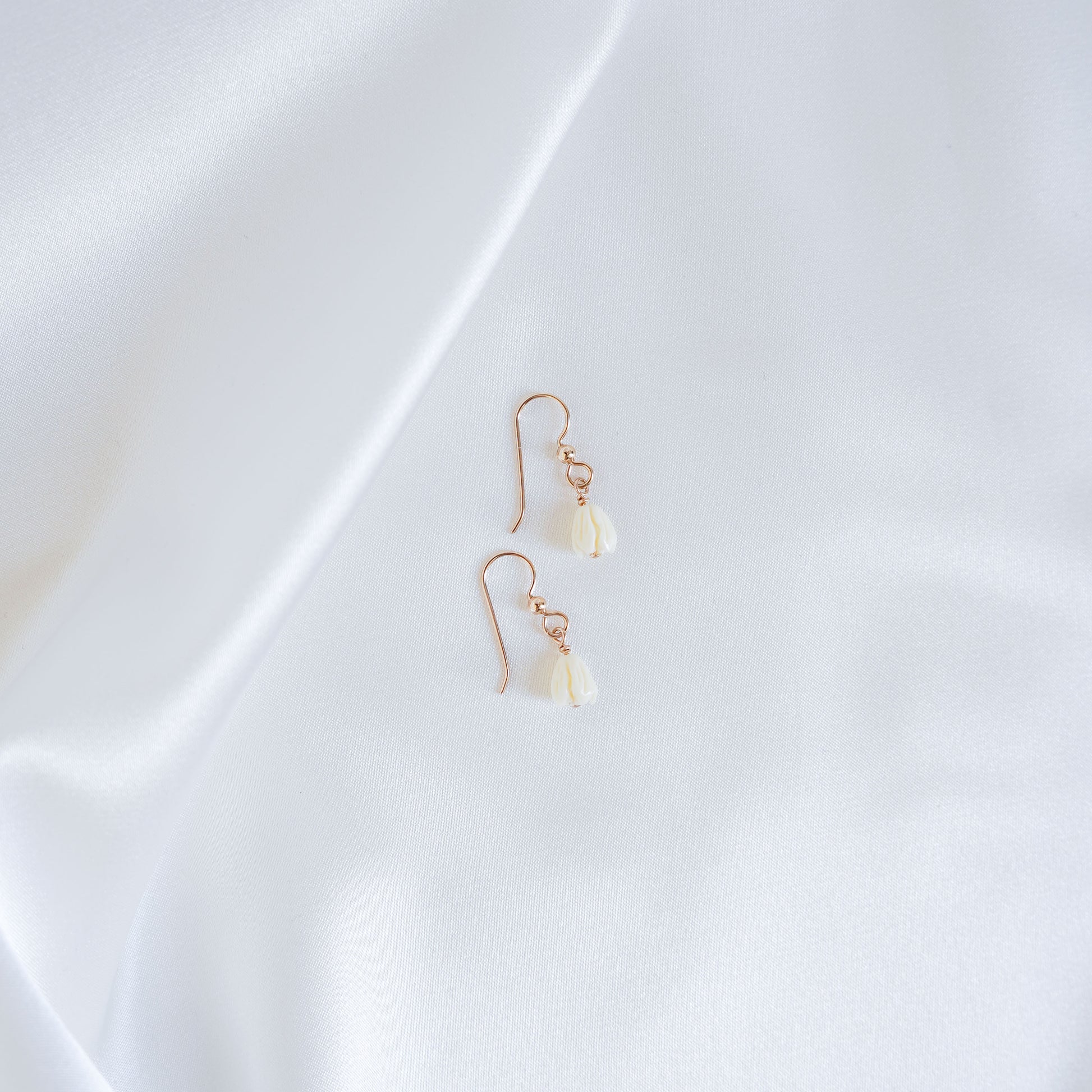Pair of gold earrings with white pikake flower beads on a white fabric background