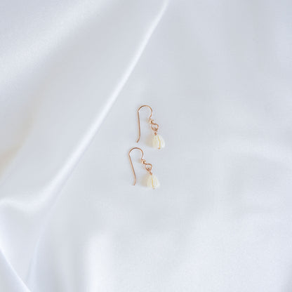 Pair of gold earrings with white pikake flower beads on a white fabric background