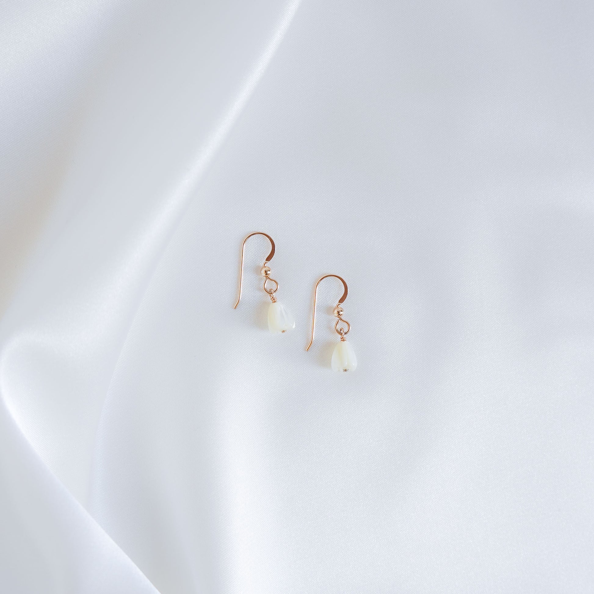 Pair of gold earrings with white pikake flower beads on a white background