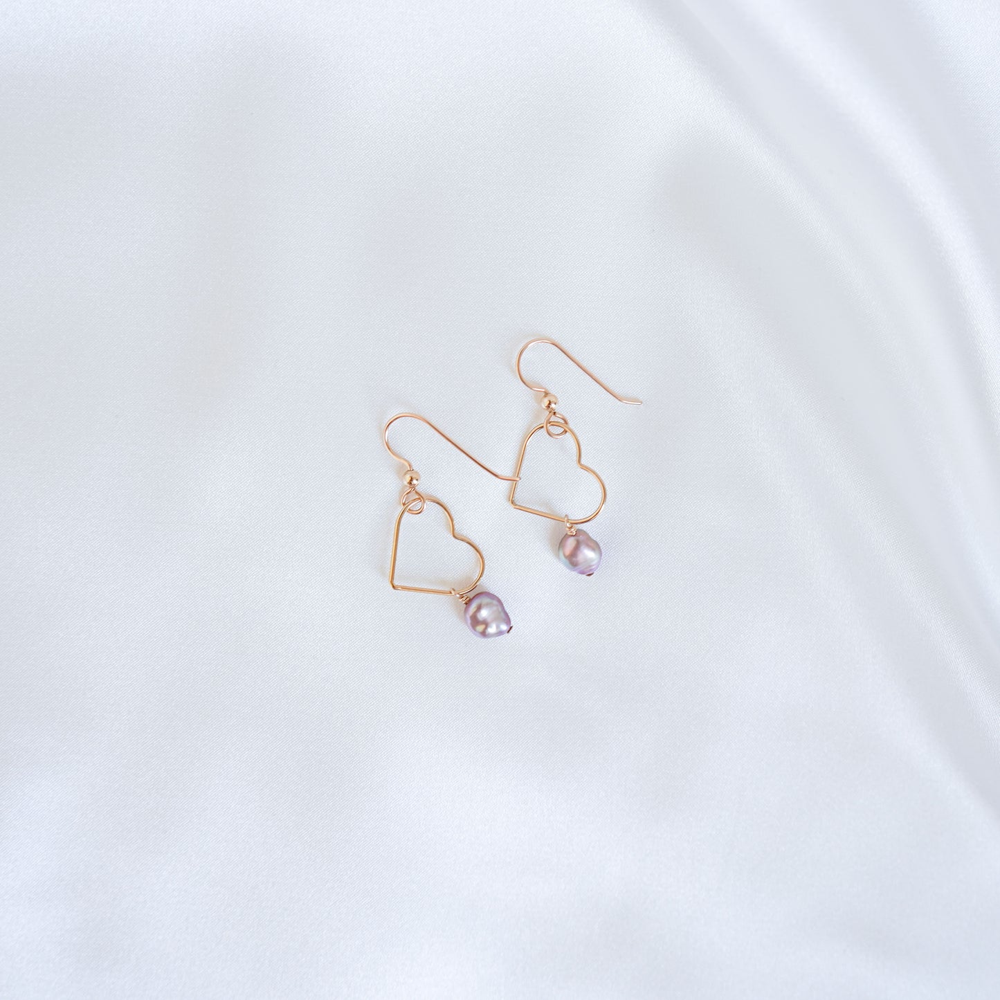 Gold heart-shaped earrings with pink keshi pearls on a white background