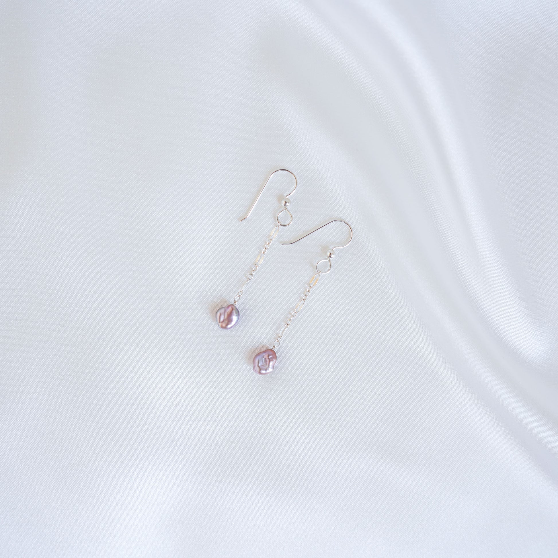 Pair of silver earrings with pink keshi pearls on a white background