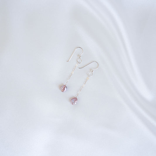 Pair of silver earrings with pink keshi pearls on a white background