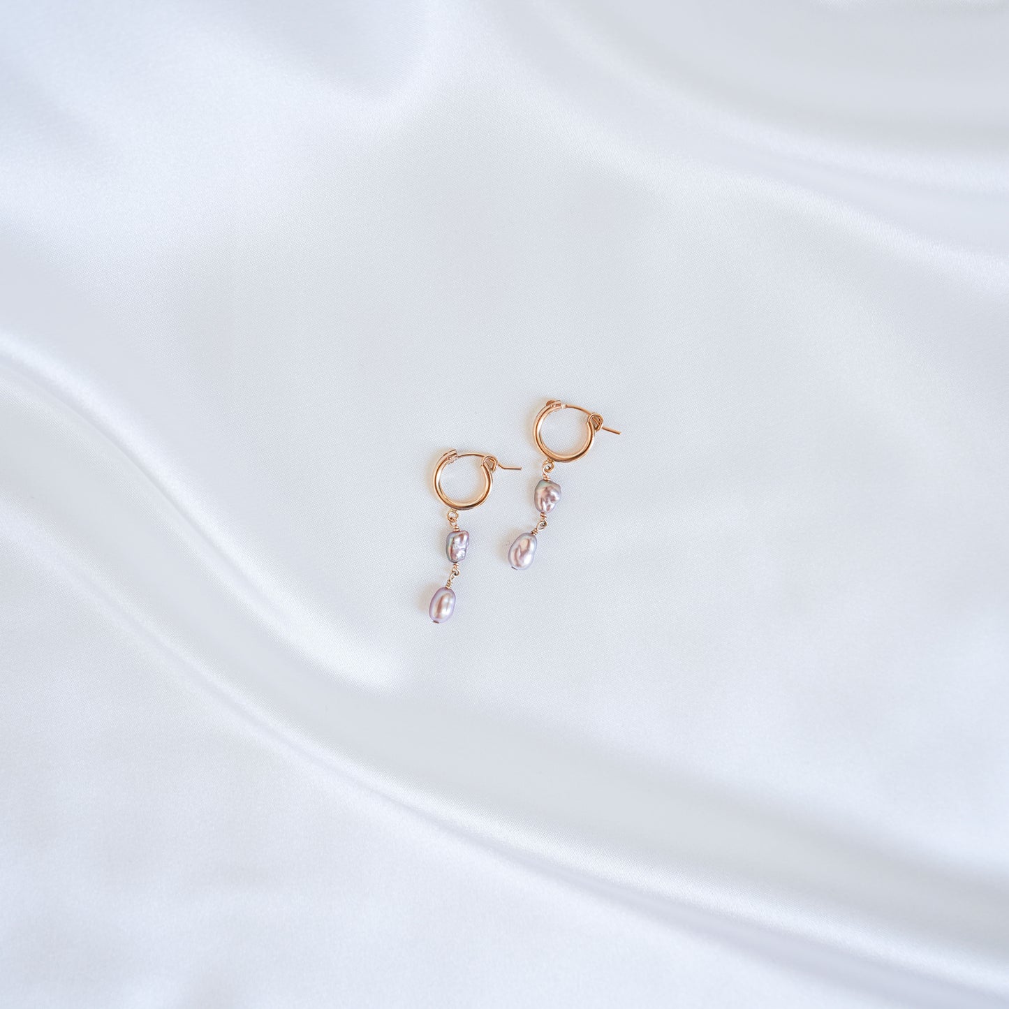 Gold earrings with pink keshi pearls on a white satin background