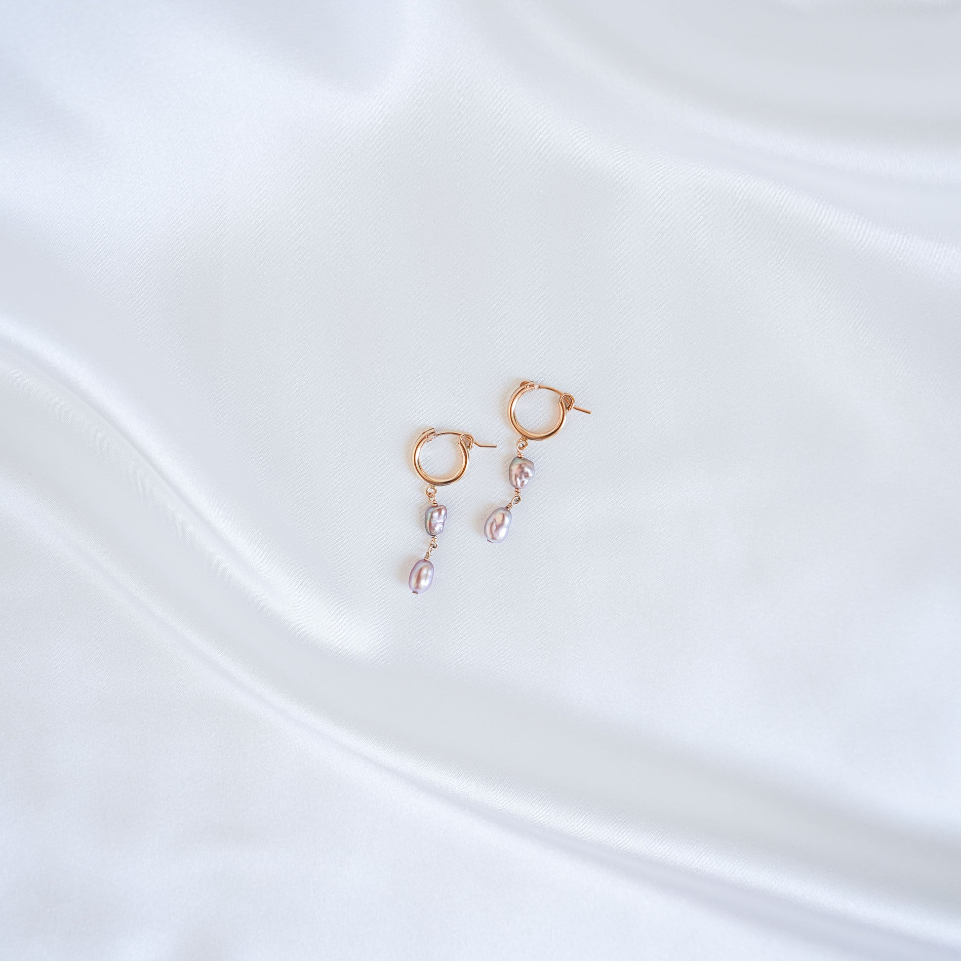Gold earrings with pink keshi pearls on a white satin background