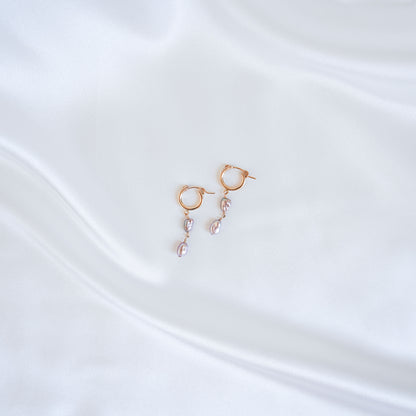Gold earrings with pink keshi pearls on a white satin background