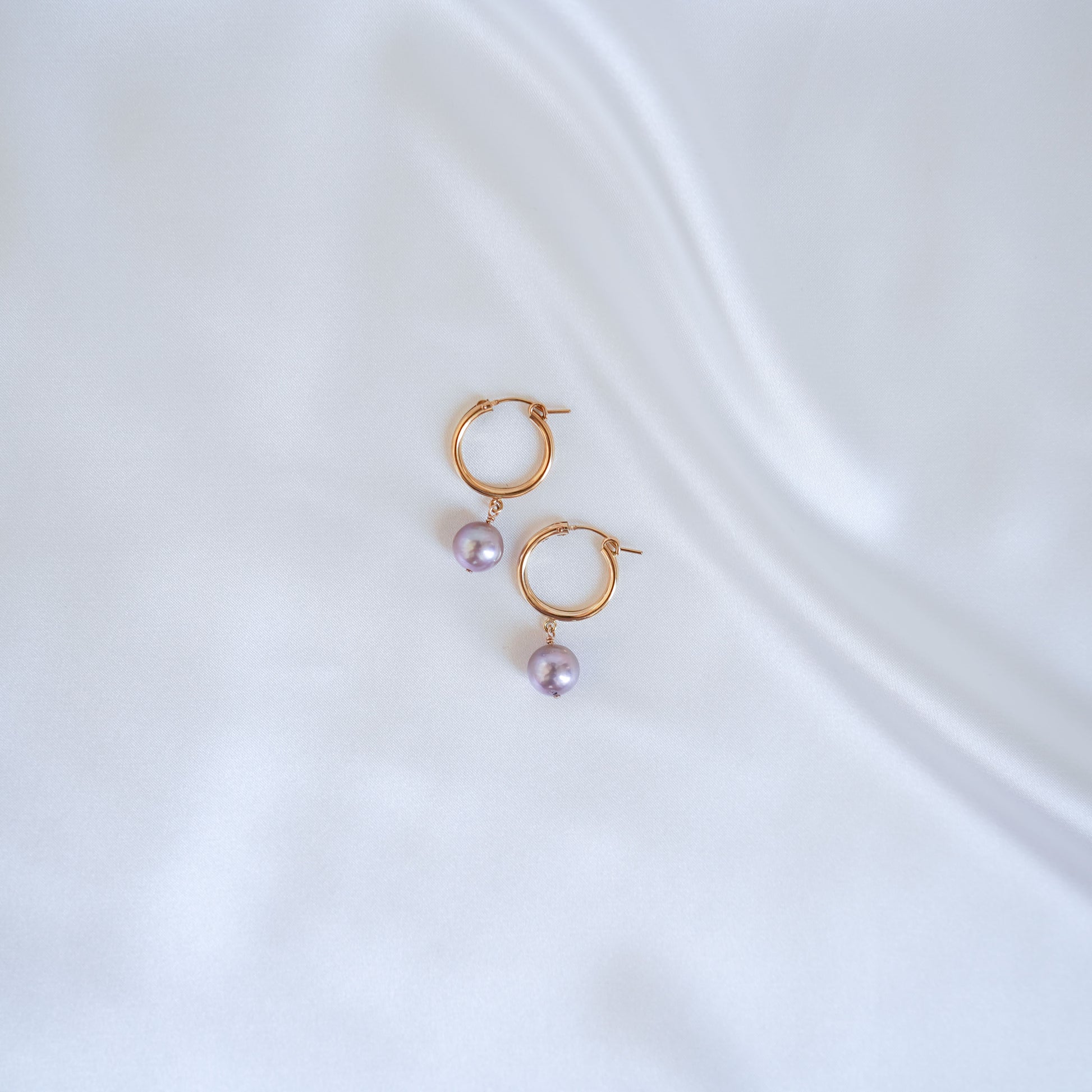 Gold hoop earrings with pink edison pearls on a white background