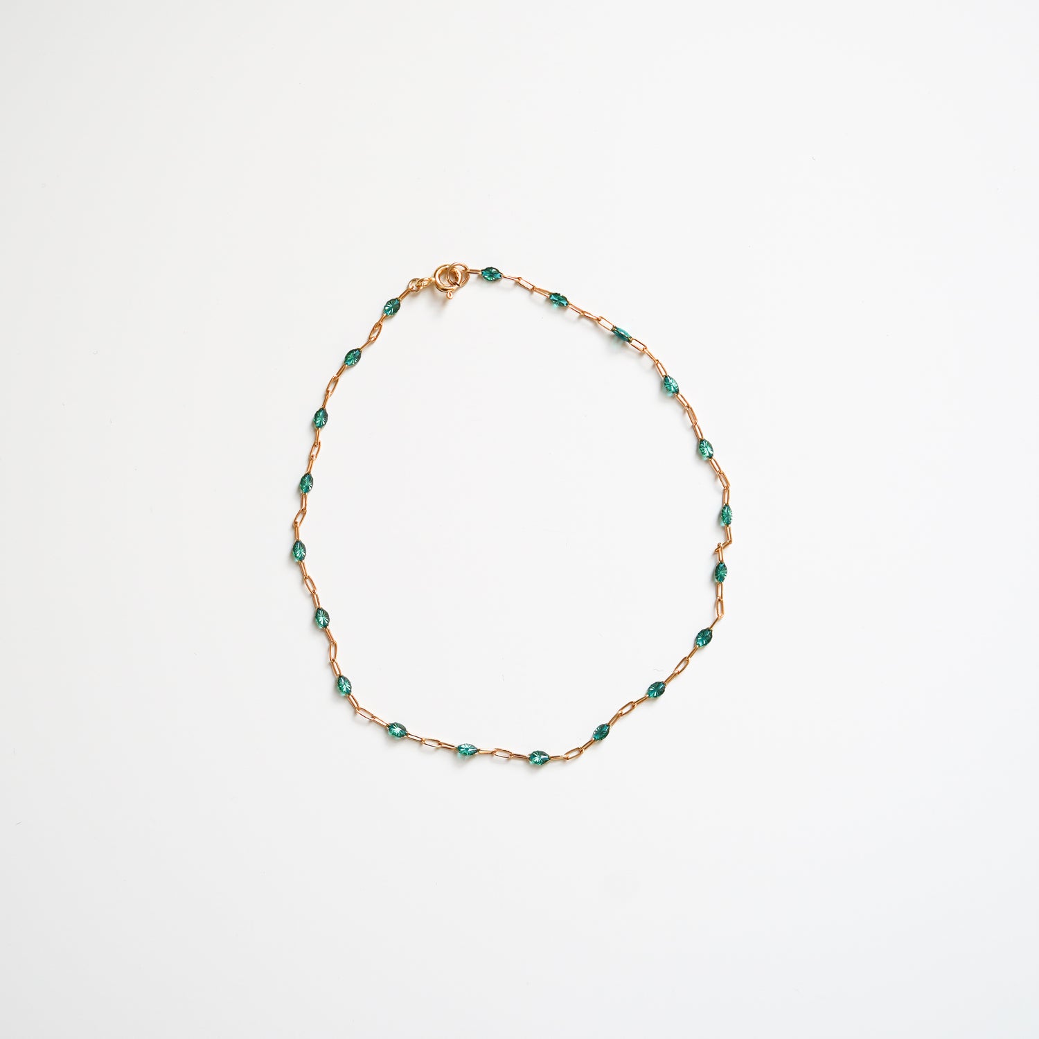 Gold chain bracelet with green stones on a white background