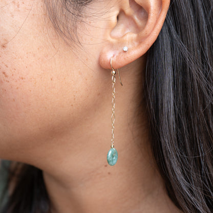 Close-up of an ear wearing a gold dangle chain earring with circle green jade with a blurred background