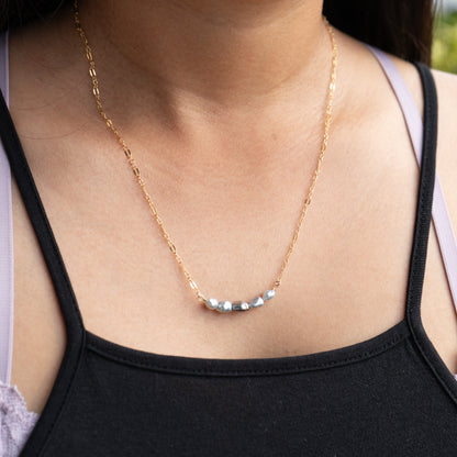 Gold necklace with five small blue pearls on a person wearing a black tank top.