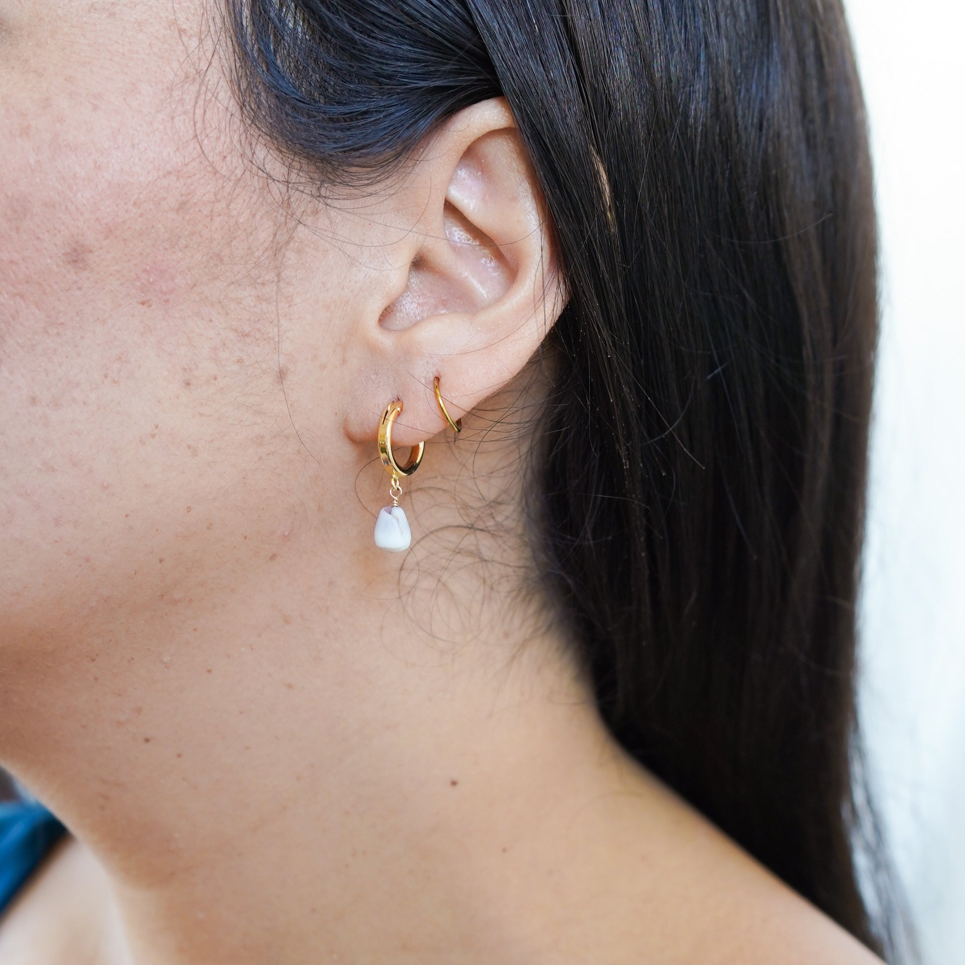 Close-up of an ear with gold hoop earrings with tiny white cone shell.