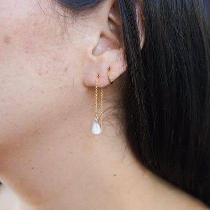 Close-up of an ear with gold chain earrings with tiny cone shell and a gold hoop earring.