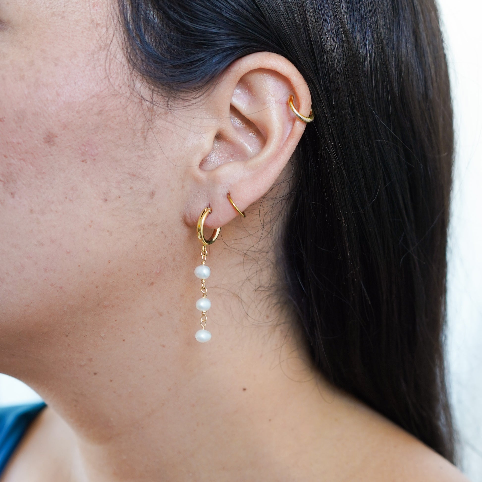 Close-up of an ear with gold hoop pearl drop earrings.