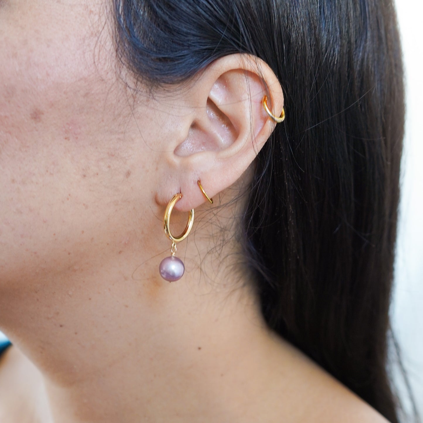 Close-up of an ear wearing gold hoop earrings with pink edison pearl.
