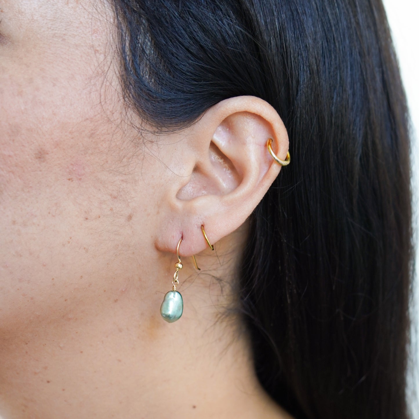 Close-up of an ear with gold hoop earrings and a green pearl earring.