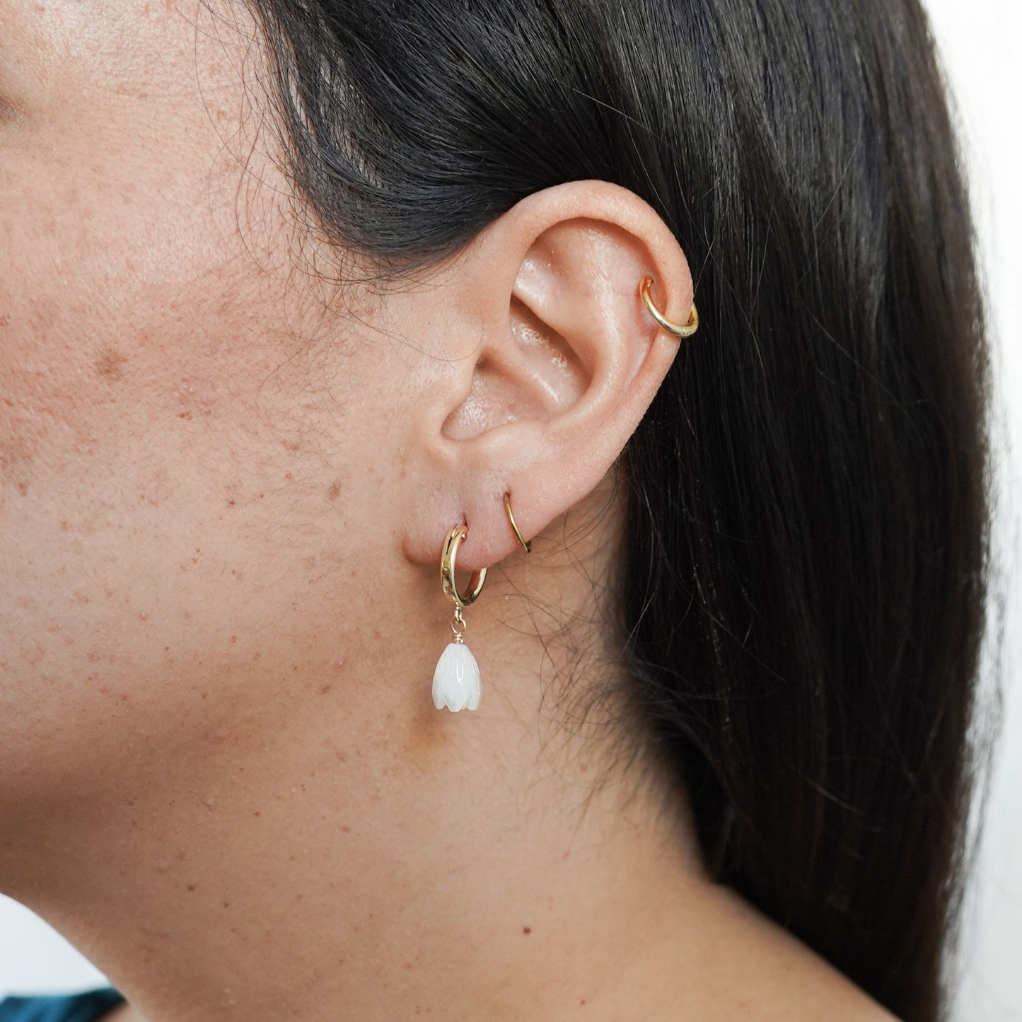 Close-up of an ear wearing gold hoop earrings with a white pikake flower bead.