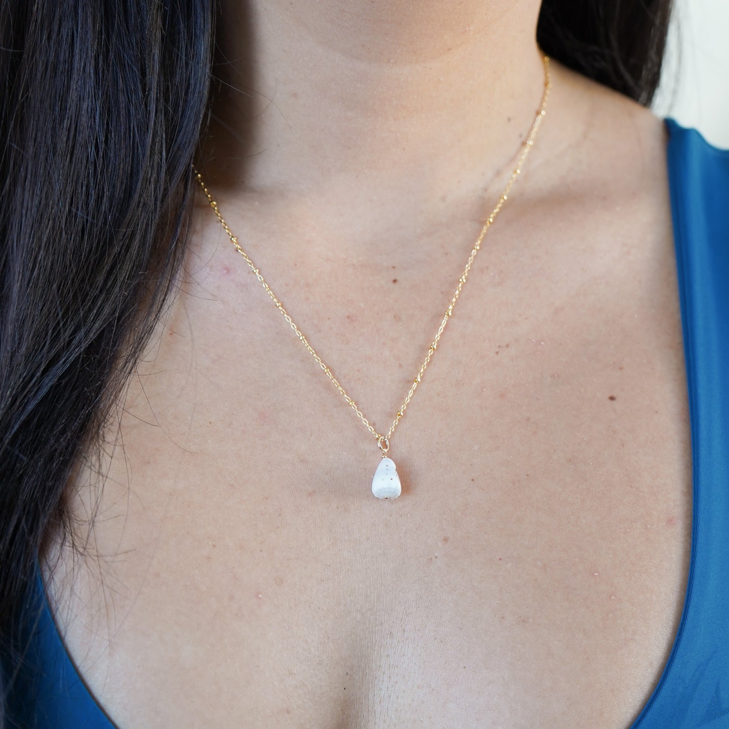 Gold necklace with a tiny white cone shell worn by a person