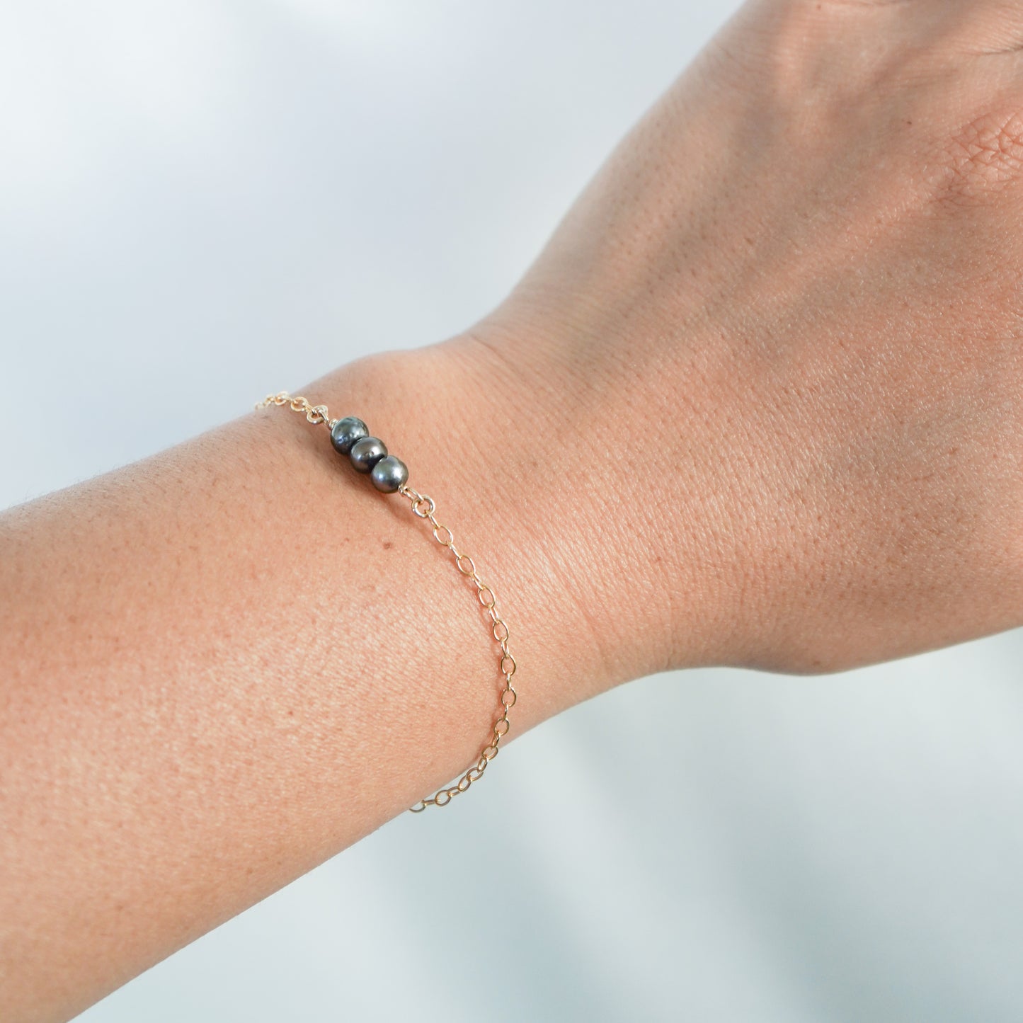 Gold bracelet with three tahitian keshi pearls on a wrist against a light background