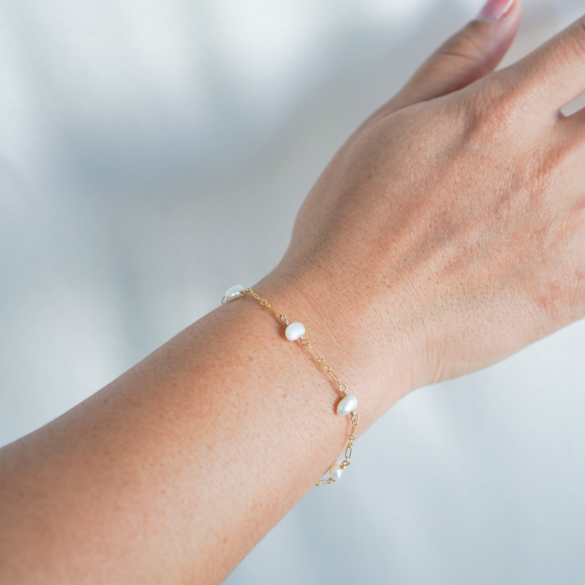 Hand wearing a delicate gold bracelet with small pearls against a blurred background