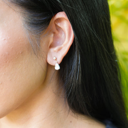 Close-up of an ear wearing a delicate CZ earring stud with tiny cone shell with a blurred green background