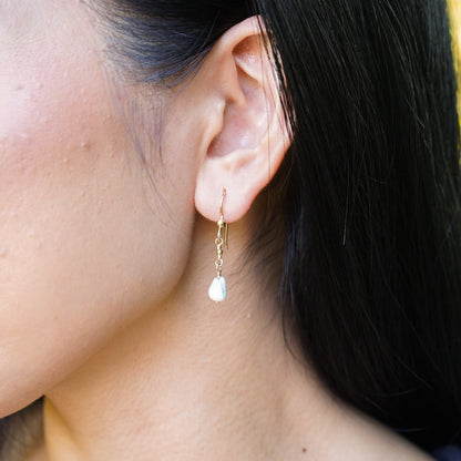 Close-up of an ear wearing a gold simple earring with a single tiny cone shell.