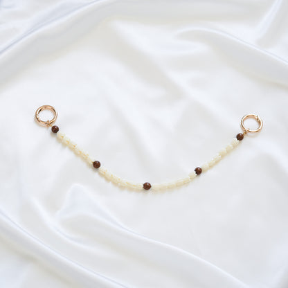 Delicate bag lei featuring white pikake flower beads and dark brown circle beads with gold rings on either end on a white fabric background