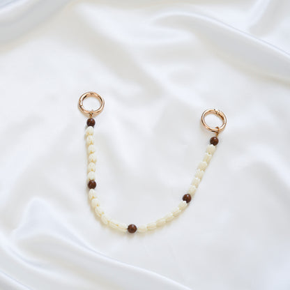 Delicate bag lei featuring white pikake flower beads and dark brown circle beads with gold rings on either end on a white fabric background