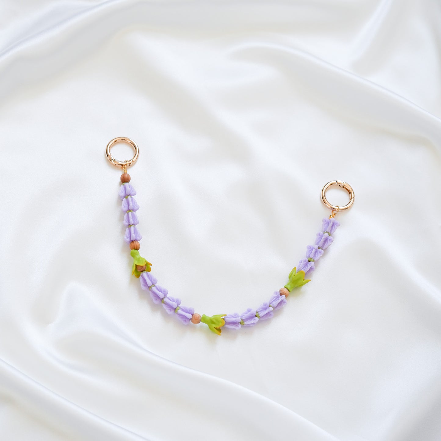 Delicate bag lei featuring purple crown flower beads and three green pakalana flower beads on a white fabric background