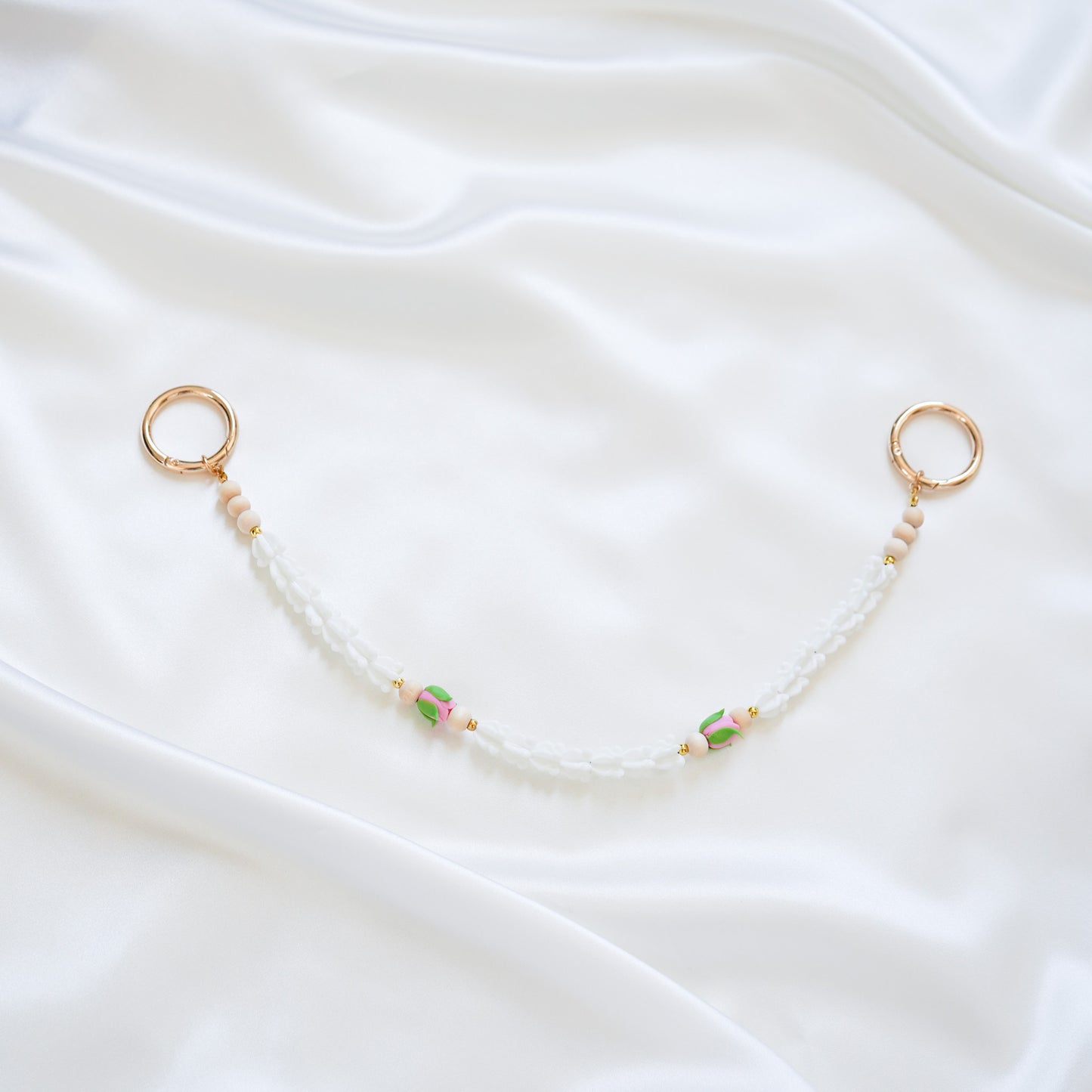 Delicate bag lei featuring white crown flower and two pink rose beads with gold rings on each end on a white fabric background