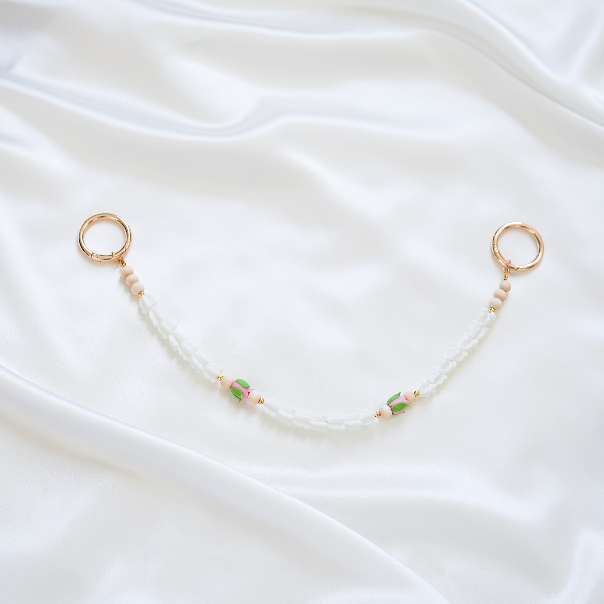 Delicate bag lei featuring white crown flower and two pink rose beads with gold rings on each end on a white fabric background