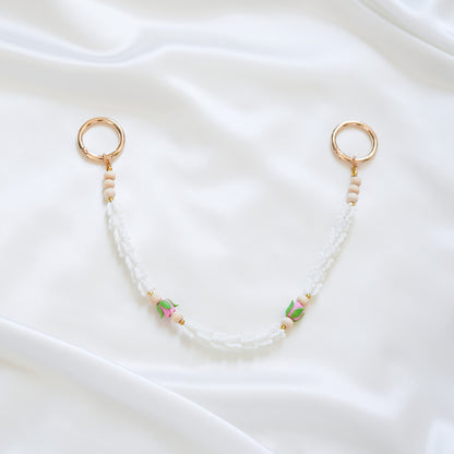 Delicate bag lei featuring white crown flower and two pink rose beads with gold rings on each end on a white fabric background