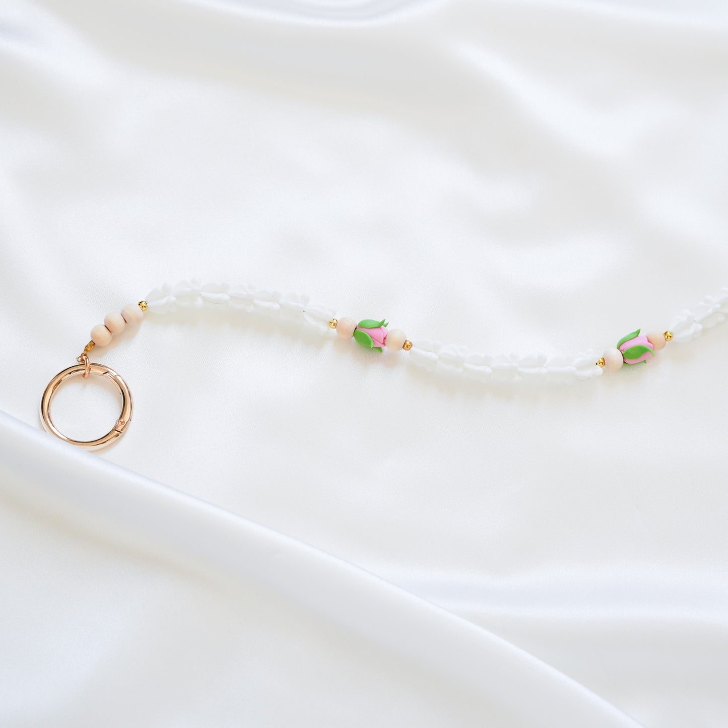 Delicate bag lei featuring white crown flower and two pink rose beads with gold rings on each end on a white fabric background