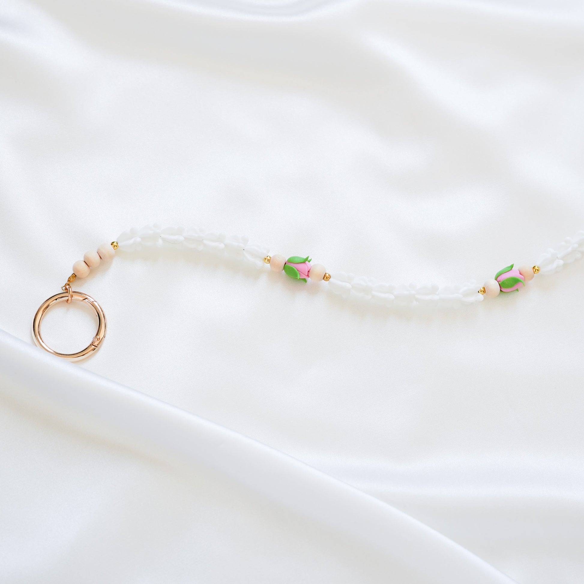 Delicate bag lei featuring white crown flower and two pink rose beads with gold rings on each end on a white fabric background