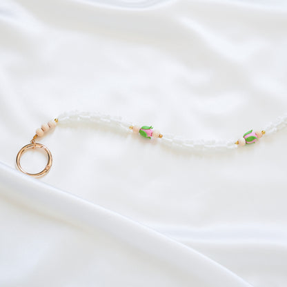 Delicate bag lei featuring white crown flower and two pink rose beads with gold rings on each end on a white fabric background