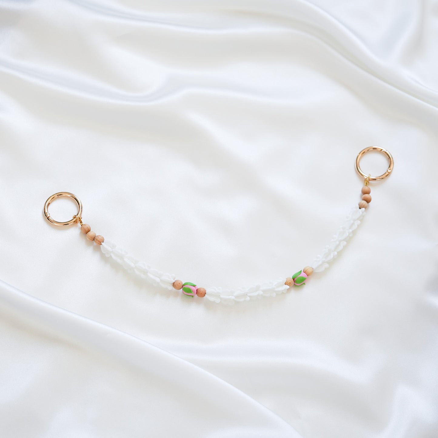 Delicate bag lei featuring white crown flower and two pink rose beads with gold rings on each end on a white fabric background