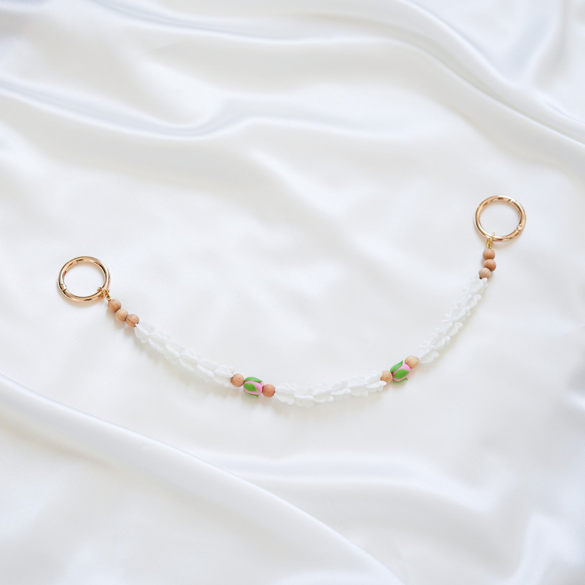 Delicate bag lei featuring white crown flower and two pink rose beads with gold rings on each end on a white fabric background